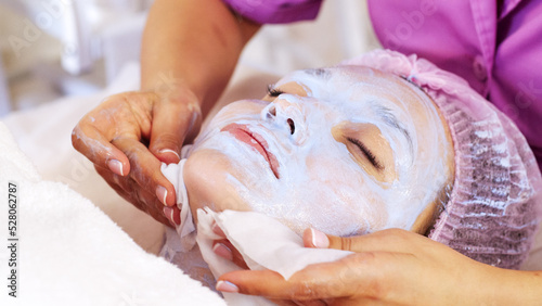 Cosmetologist removing  a mask scrub from female face. Woman in a spa salon on cosmetic procedures for facial care.