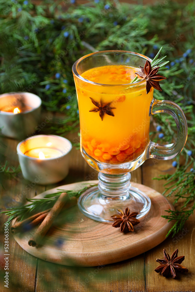 hot warming autumn sea buckthorn tea with cinnamon and star anise spices in a transparent cup stands on a wooden background. antivirus drink. Herbal vitamin tea. Hot autumn drink. Christmas drink