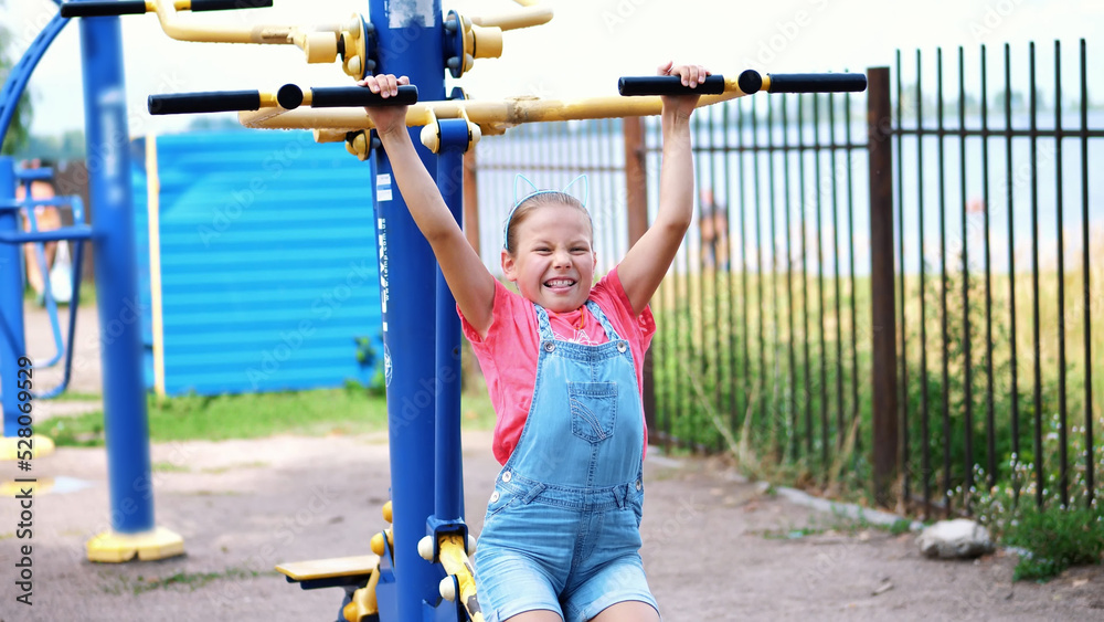 smiling, happy eight year old girl engaged, doing exercises on outdoor exercise equipment, outdoors, in the park, summer, hot day during the holidays. High quality photo smiling, happy eight year old girl engaged, doing exercises on outdoor exercise equipment, outdoors, in the park, summer, hot day during the holidays. High quality photo