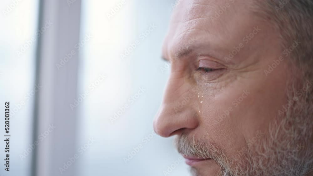 Depressed man in his 50s crying while looking out the window, betrayal and hurt Depressed man in his 50s crying while looking out the window, betrayal and hurt