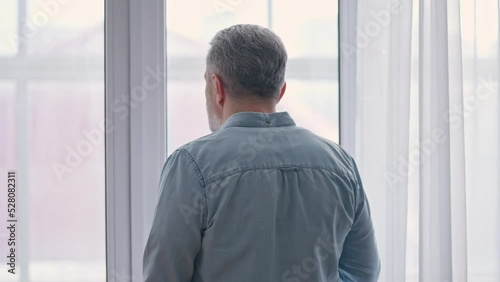 Sad middle-aged male drinking tea and looking out the window, midlife crisis photo