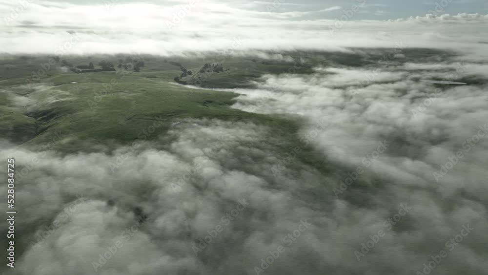 Flying above clouds over hills. above fog on a farm landscape below. mist covering the mountains in the country Flying above clouds over hills. above fog on a farm landscape below. mist covering the mountains in the country