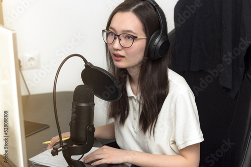 Young woman with glasses, microphone and headphones recording podcast at studio, professional record audio, technology and media concept