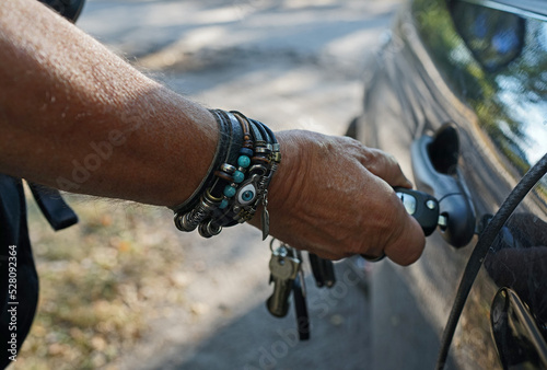 Man opening his car with a car key. He wears a lot of leather bracelets
