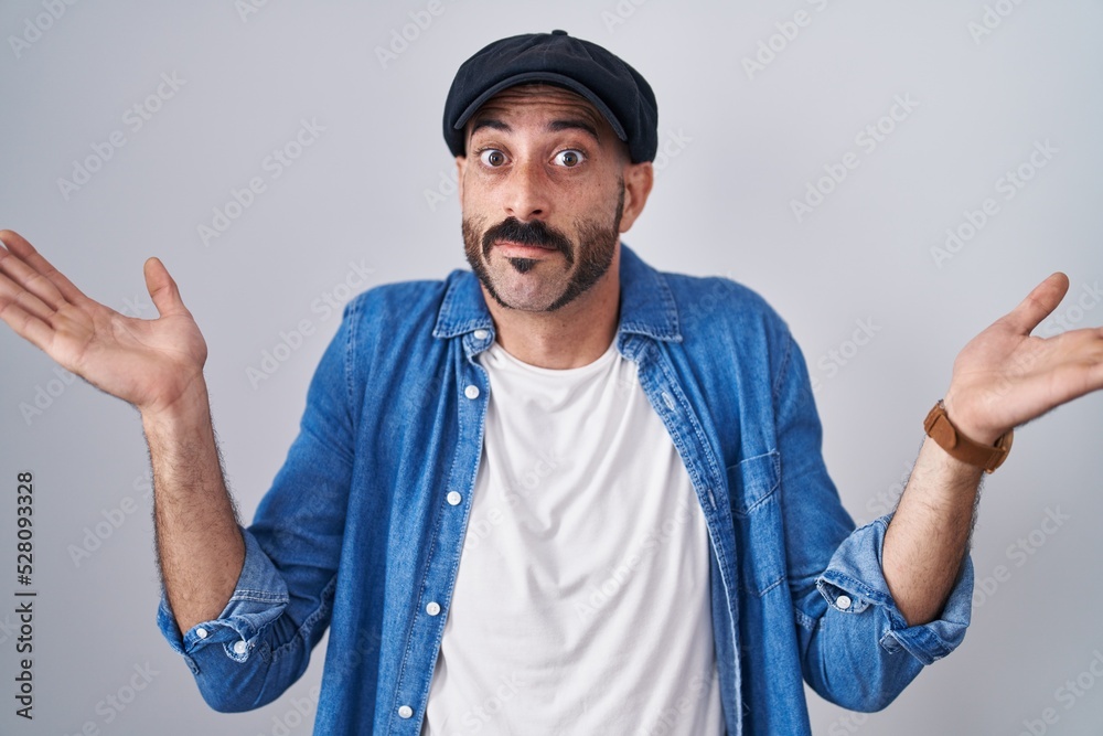 Hispanic man with beard standing over isolated background clueless and confused expression with arms and hands raised. doubt concept. Hispanic man with beard standing over isolated background clueless and confused expression with arms and hands raised. doubt concept.