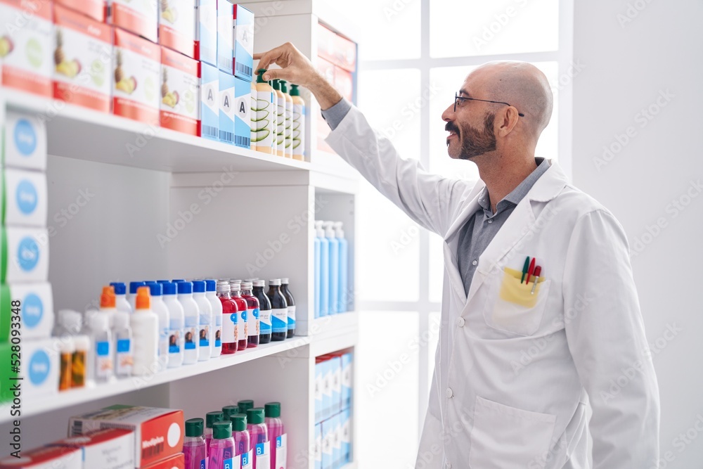 Young hispanic man pharmacist smiling confident holding bottle at pharmacy