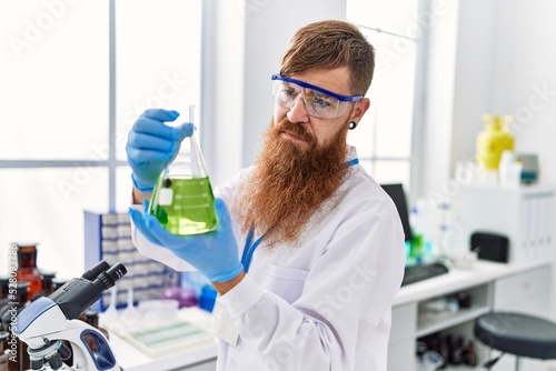 Young redhead man wearing scientist uniform holding test tube at laboratory