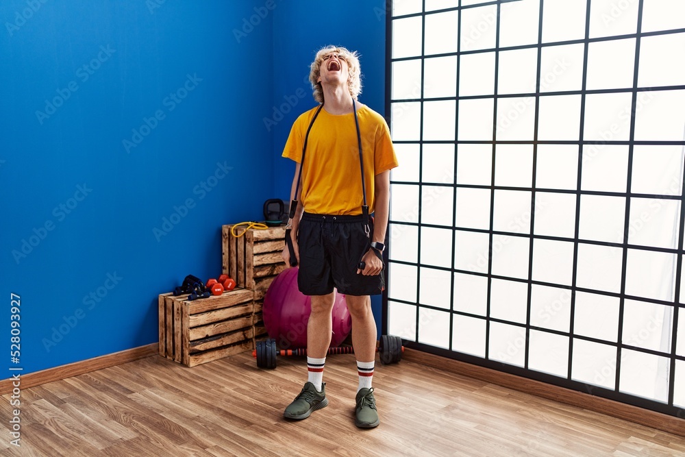 Young man training arm resistance with elastic arm bands angry and mad screaming frustrated and furious, shouting with anger looking up. Young man training arm resistance with elastic arm bands angry and mad screaming frustrated and furious, shouting with anger looking up.