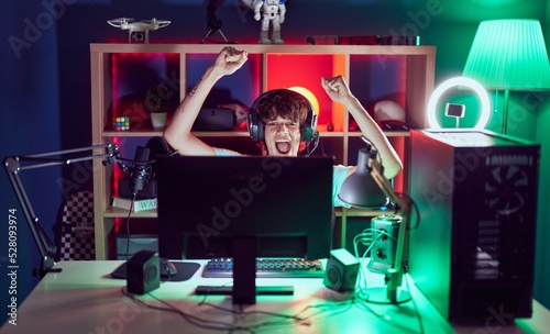 Young blond man streamer playing video game with winner expression at gaming room