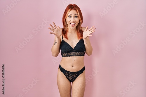 Young caucasian woman wearing lingerie over pink background celebrating crazy and amazed for success with arms raised and open eyes screaming excited. winner concept