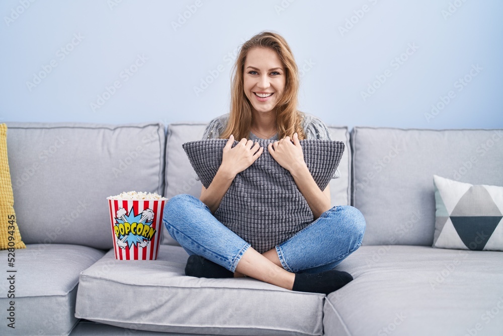 Beautiful blonde woman watching tv sitting on the sofa smiling with a happy and cool smile on face. showing teeth. Beautiful blonde woman watching tv sitting on the sofa smiling with a happy and cool smile on face. showing teeth.