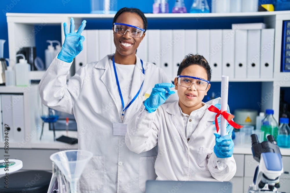 Mother and son at scientist laboratory doing ok sign with fingers, smiling friendly gesturing excellent symbol Mother and son at scientist laboratory doing ok sign with fingers, smiling friendly gesturing excellent symbol