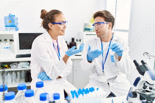 Man and woman wearing scientist uniform holding sample talking at laboratory