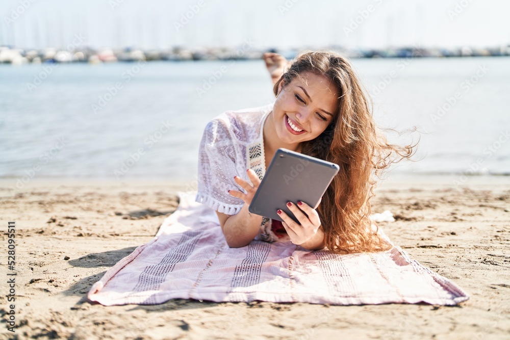 Young beautiful hispanic woman tourist using touchpad lying on sand at beach