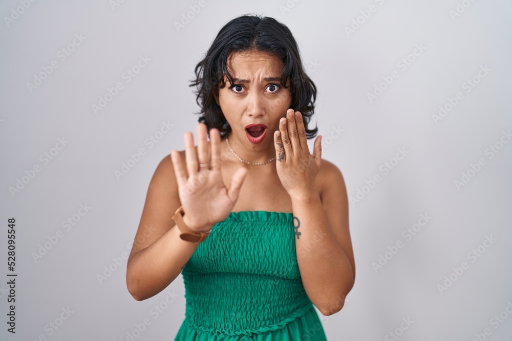 Young hispanic woman standing over isolated background moving away hands palms showing refusal and denial with afraid and disgusting expression. stop and forbidden. Young hispanic woman standing over isolated background moving away hands palms showing refusal and denial with afraid and disgusting expression. stop and forbidden.