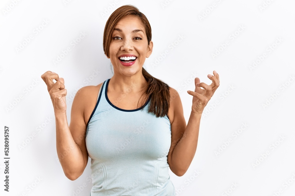 Young latin woman wearing sporty clothes over isolated background celebrating surprised and amazed for success with arms raised and open eyes. winner concept. Young latin woman wearing sporty clothes over isolated background celebrating surprised and amazed for success with arms raised and open eyes. winner concept.