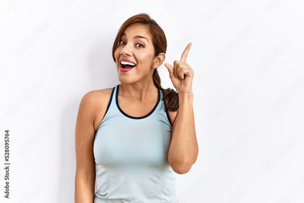 Young latin woman wearing sporty clothes over isolated background pointing finger up with successful idea. exited and happy. number one. Young latin woman wearing sporty clothes over isolated background pointing finger up with successful idea. exited and happy. number one.