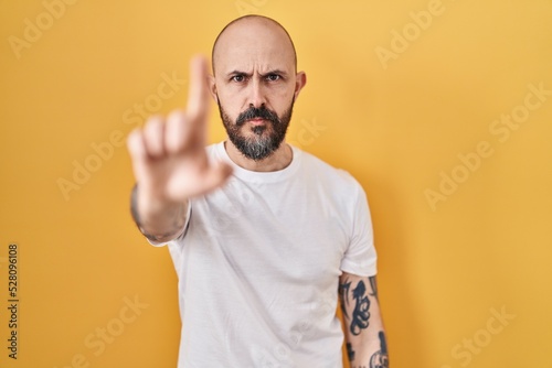 Young hispanic man with tattoos standing over yellow background pointing with finger up and angry expression, showing no gesture © Krakenimages.com