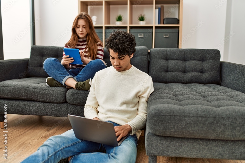 Young couple with serious expression using laptop and touchpad sitting on the sofa at home. Young couple with serious expression using laptop and touchpad sitting on the sofa at home.