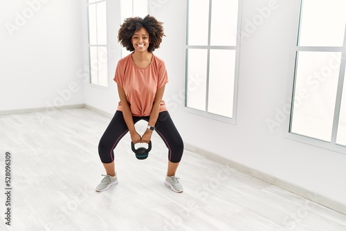 Young african american woman smiling confident training using kettlebell at sport center