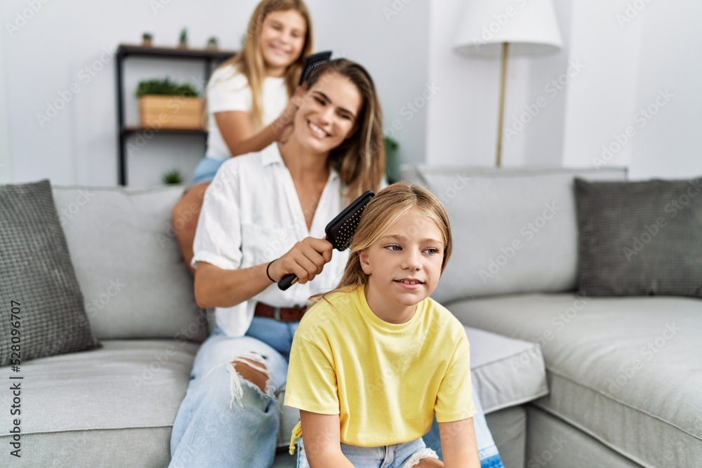 Mother and daughters smiling confident combing hair at home