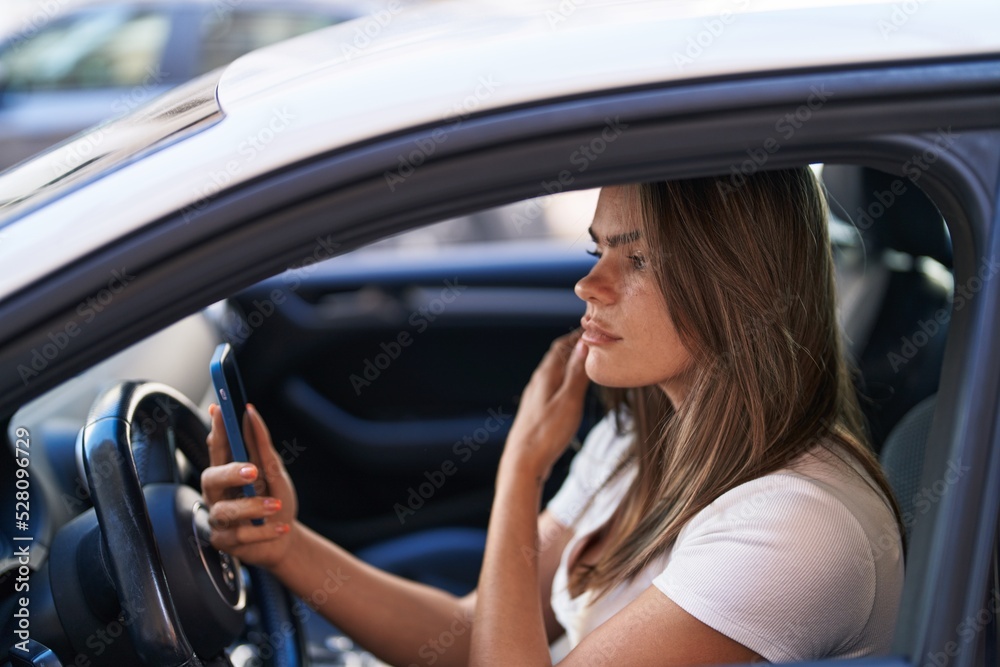 Young woman talking on the smartphone sitting on car at street