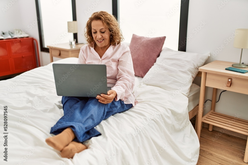 Middle age caucasian woman using laptop sitting on the bed at bedroom. Middle age caucasian woman using laptop sitting on the bed at bedroom.