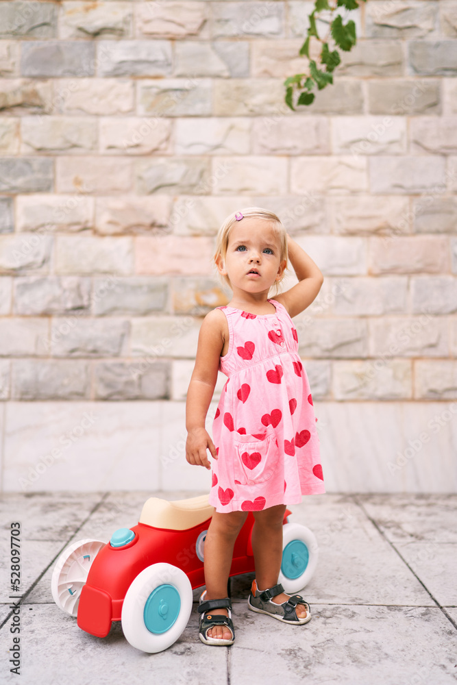 Fototapeta premium Little girl stands and looks up near a toy car. High quality photo