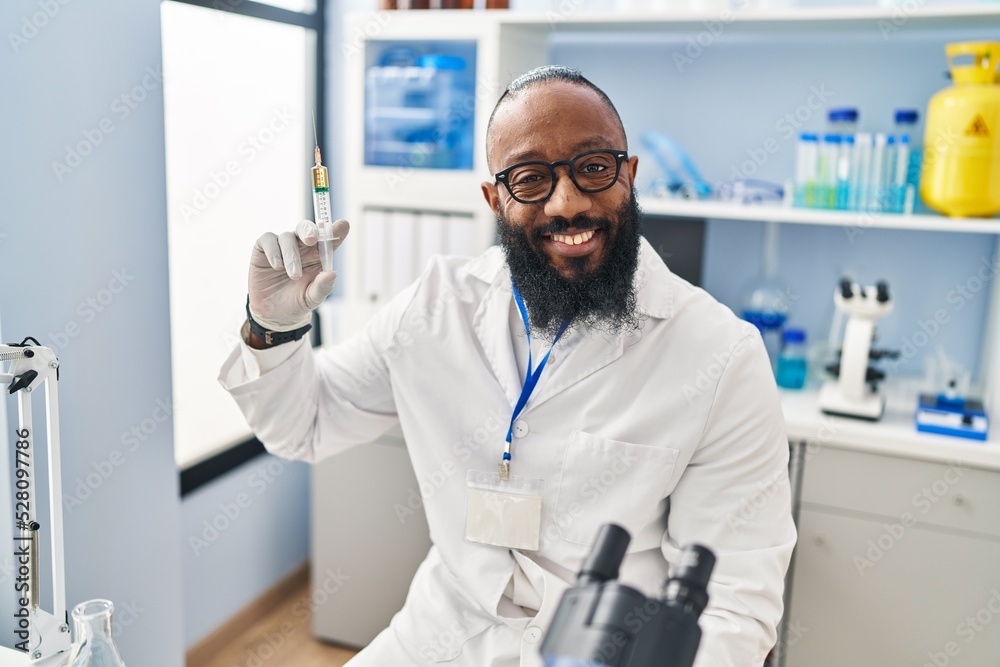 African american man working at scientist laboratory holding syringe looking positive and happy standing and smiling with a confident smile showing teeth African american man working at scientist laboratory holding syringe looking positive and happy standing and smiling with a confident smile showing teeth