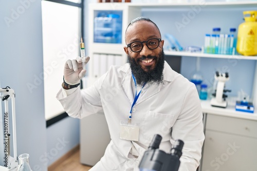 African american man working at scientist laboratory holding syringe looking positive and happy standing and smiling with a confident smile showing teeth