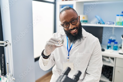 Young african american man wearing scientist uniform holding diamond at laboratory
