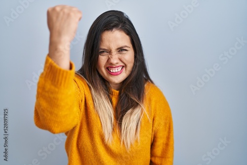 Young hispanic woman standing over isolated background angry and mad raising fist frustrated and furious while shouting with anger. rage and aggressive concept. © Krakenimages.com