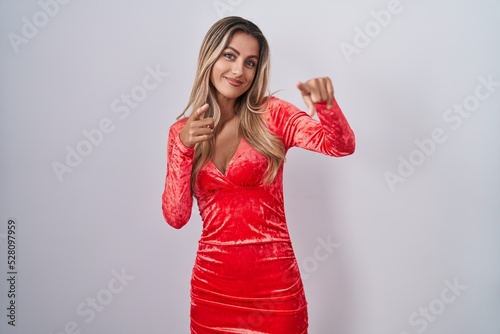 Young blonde woman wearing sexy party dress pointing fingers to camera with happy and funny face. good energy and vibes.