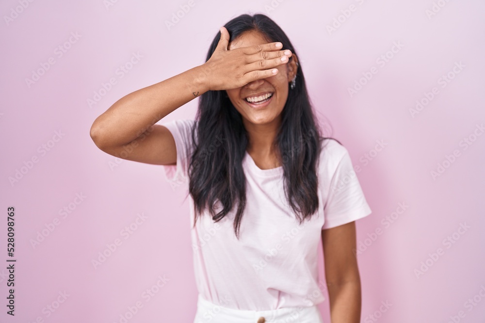 Young hispanic woman standing over pink background smiling and laughing with hand on face covering eyes for surprise. blind concept. Young hispanic woman standing over pink background smiling and laughing with hand on face covering eyes for surprise. blind concept.