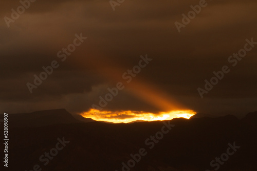 Dark cloudscape. View of the dramatic sunset with dark clouds. The last bright ray of sunlight strikes across the sky and mountains silhouette.