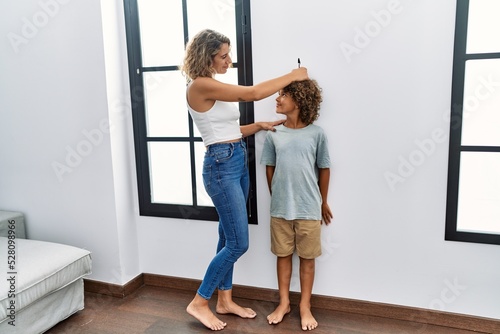 Mother and son measuring child height drawing mark on wall at home