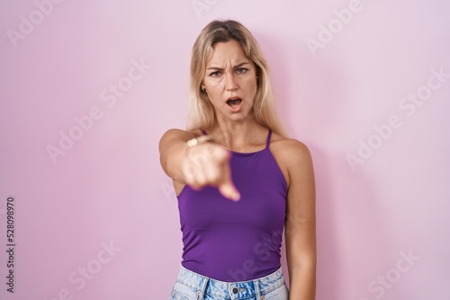 Young blonde woman standing over pink background pointing displeased and frustrated to the camera  angry and furious with you