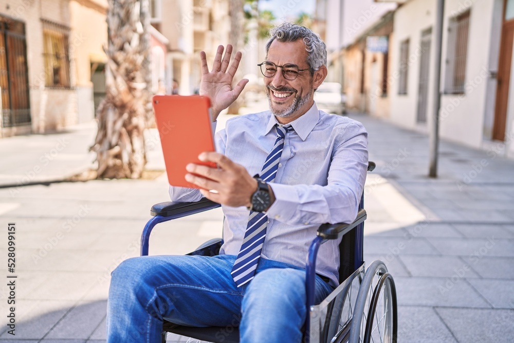 Middle age hispanic man sitting on wheelchair having video call at street