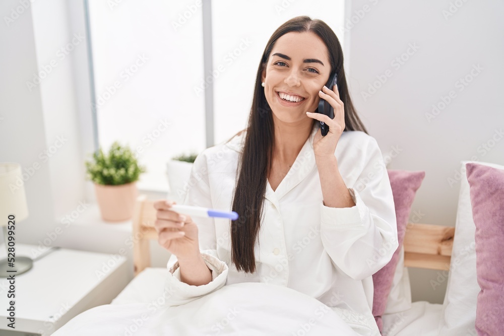 Young hispanic woman talking on the smartphone holding pregnancy test at bedroom Young hispanic woman talking on the smartphone holding pregnancy test at bedroom