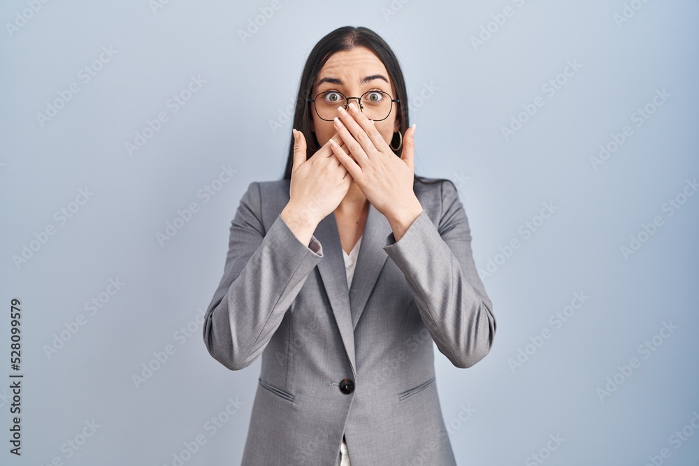 Hispanic business woman wearing glasses shocked covering mouth with hands for mistake. secret concept. Hispanic business woman wearing glasses shocked covering mouth with hands for mistake. secret concept.