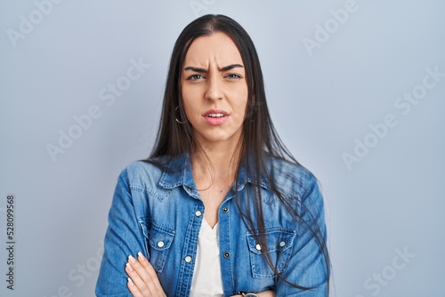 Hispanic woman standing over blue background skeptic and nervous, disapproving expression on face with crossed arms. negative person.