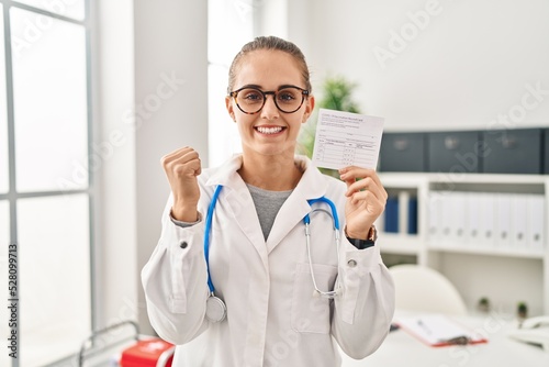 Young doctor woman holding covid certificate screaming proud  celebrating victory and success very excited with raised arms