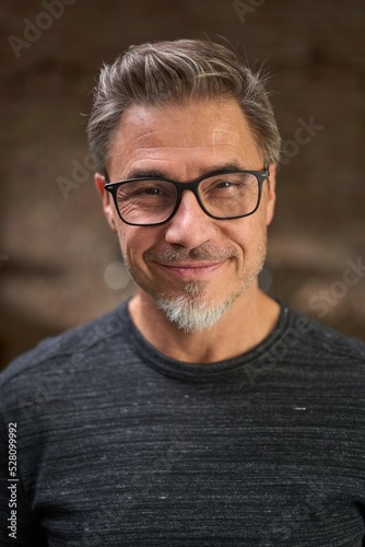 Portrait of happy middle aged man in a dark industrial room wearing glasses, smiling.