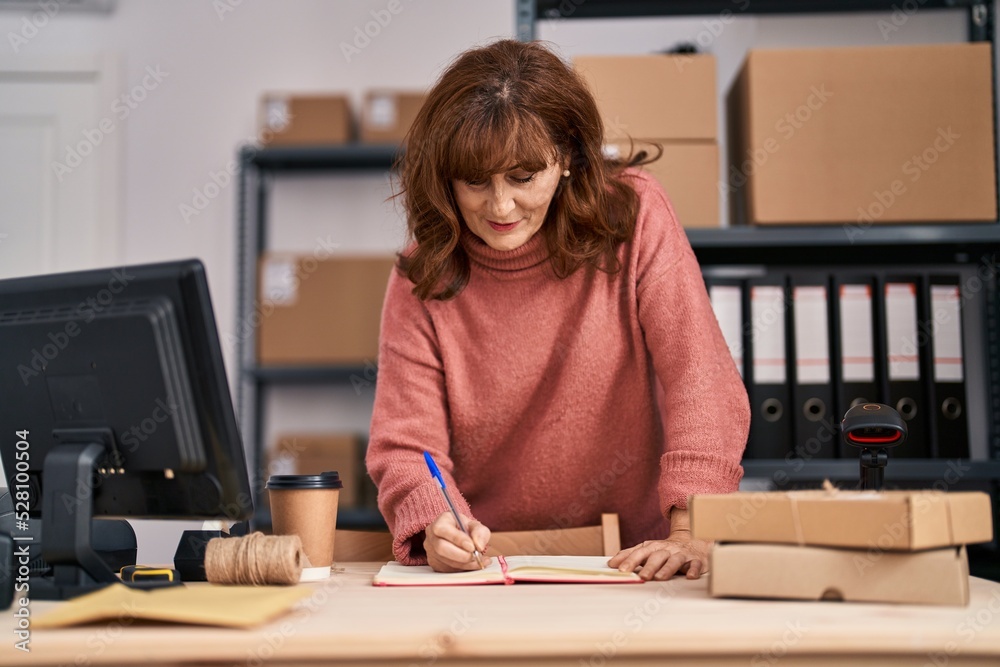 Middle age woman ecommerce business worker writing on book at office Middle age woman ecommerce business worker writing on book at office