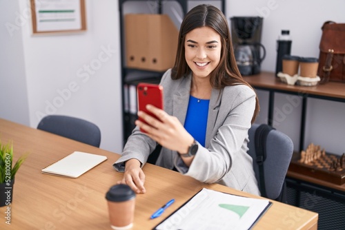 Young beautiful hispanic woman business worker make selfie by smartphone at office