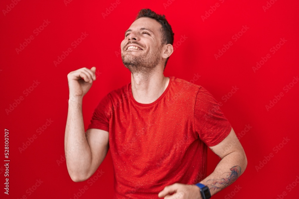 Young hispanic man standing over red background dancing happy and cheerful, smiling moving casual and confident listening to music Young hispanic man standing over red background dancing happy and cheerful, smiling moving casual and confident listening to music