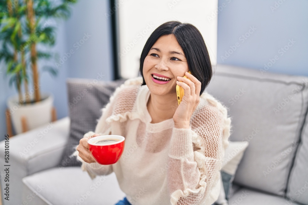 Young chinese woman drinking coffee and talking on the smartphone at home Young chinese woman drinking coffee and talking on the smartphone at home
