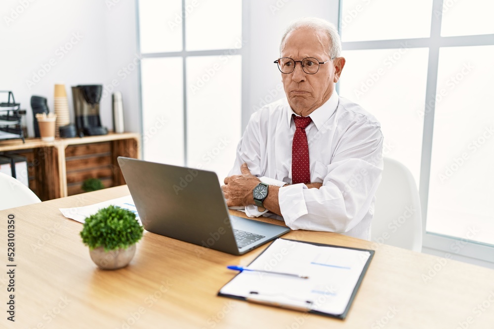 Senior man working at the office using computer laptop skeptic and nervous, disapproving expression on face with crossed arms. negative person. Senior man working at the office using computer laptop skeptic and nervous, disapproving expression on face with crossed arms. negative person.