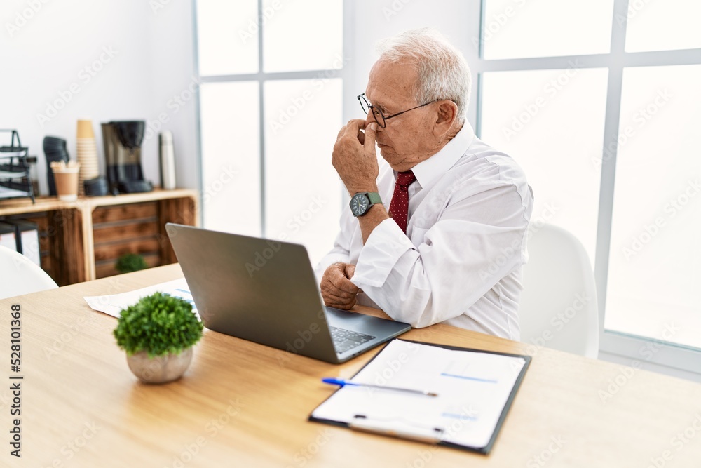 Senior man working at the office using computer laptop tired rubbing nose and eyes feeling fatigue and headache. stress and frustration concept. Senior man working at the office using computer laptop tired rubbing nose and eyes feeling fatigue and headache. stress and frustration concept.