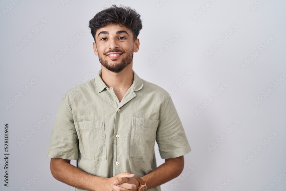 Arab man with beard standing over white background with hands together and crossed fingers smiling relaxed and cheerful. success and optimistic Arab man with beard standing over white background with hands together and crossed fingers smiling relaxed and cheerful. success and optimistic
